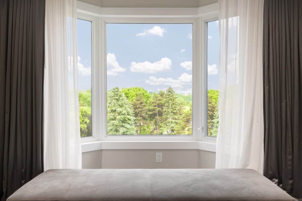 Bay window with drapes, curtains and view of trees under summer sky